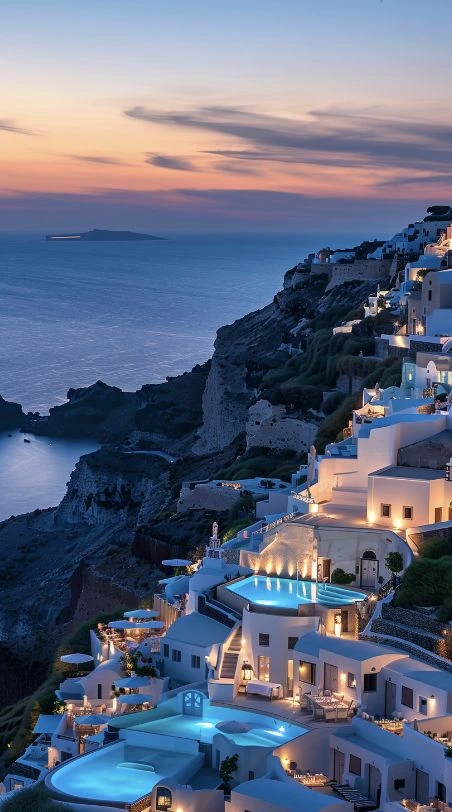 A stunning view of Santorini's iconic white-washed buildings perched on cliffs, illuminated by warm lights against a vibrant sunset sky.