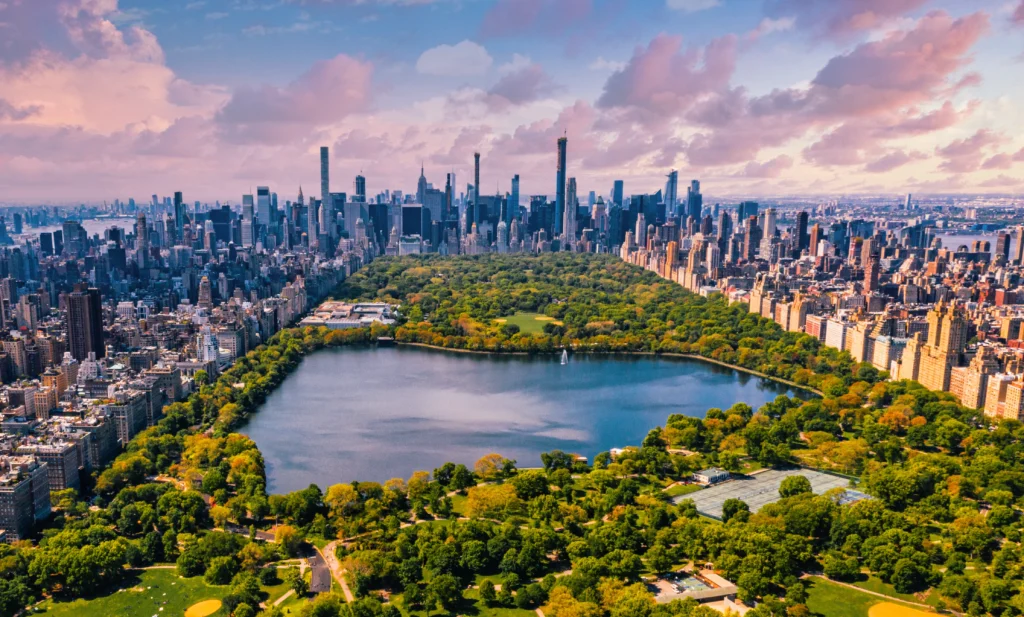 A magnificent skyline of iconic American cities, captured in a breathtaking panoramic view. In the foreground, the towering skyscrapers of New York City stand tall, their glass facades reflecting the warm glow of the setting sun. The middle ground features the distinctive silhouettes of the Chicago skyline, its iconic Willis Tower and Hancock Center piercing the sky. In the background, the dramatic peaks of the Seattle skyline rise up, the Space Needle standing as a symbol of the city's innovation and progress. The scene is bathed in a soft, golden light, creating a warm and inviting atmosphere that captures the essence of these vibrant urban landscapes. The composition is balanced and visually striking, drawing the viewer's eye across the panorama of America's most iconic cities. Best Places to Visit in USA