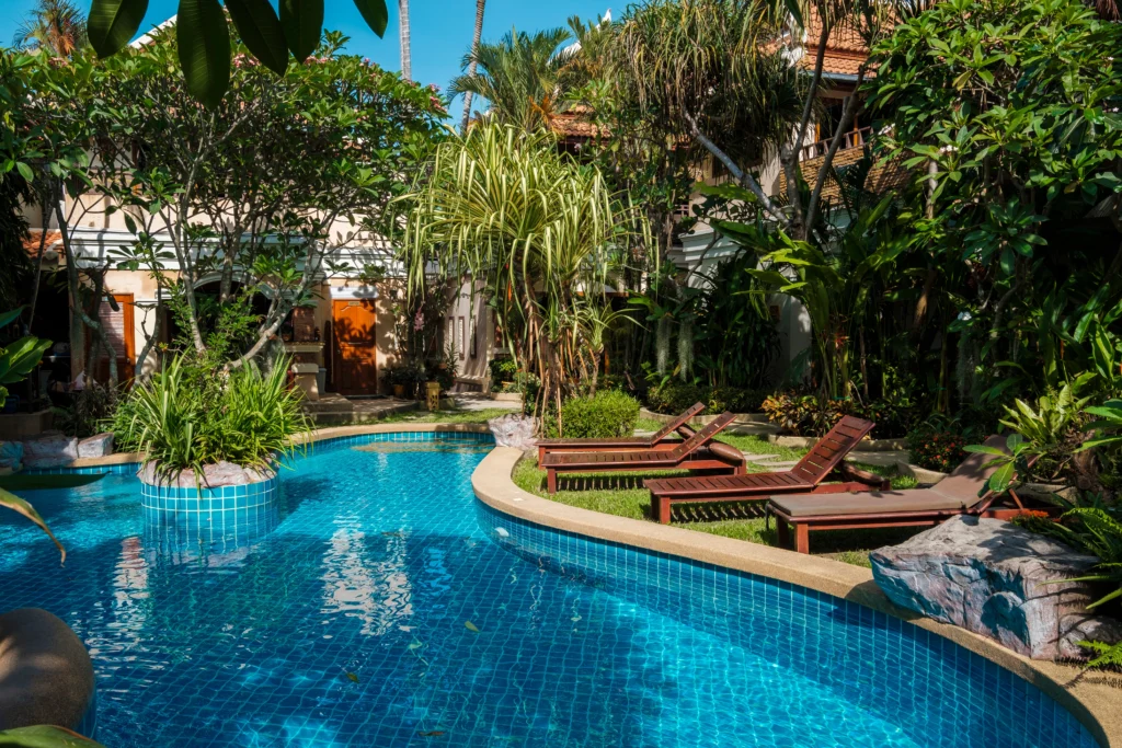 a serene tropical hotel landscape in Brazil, South America, with a lush, verdant foliage-filled foreground, a picturesque two-story hotel building with a tiled roof and balconies in the middle ground, and a backdrop of rolling hills and a clear blue sky with wispy clouds, bathed in warm, golden hour lighting, captured with a wide-angle lens to create a sense of depth and grandeur, conveying a tranquil, inviting atmosphere perfect for a relaxing getaway